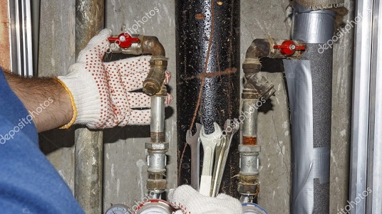plumber repairs pipes in plumbing unit. Hands plumbing with spanners on background of pipes, manometers and filters